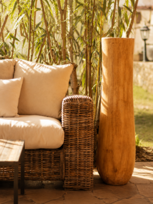 Grande bougie en tronc de palmier clair installée sur une terrasse ensoleillée dans une ambiance inspirée des villas balinaises.