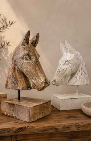 Deux bustes de cheval en bois sculpté, naturel et blanchi, présentés sur une console dans une ambiance bohème chic.