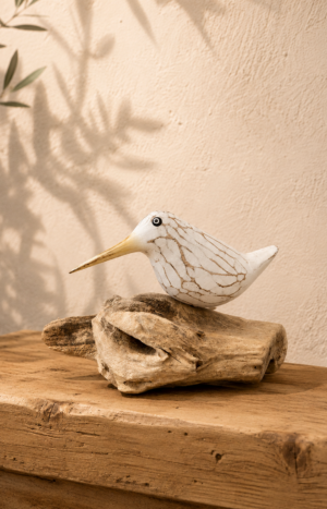 Oiseau blanc en bois sculpté avec bec jaune posé sur une branche de teck dans une ambiance bord de mer chic.