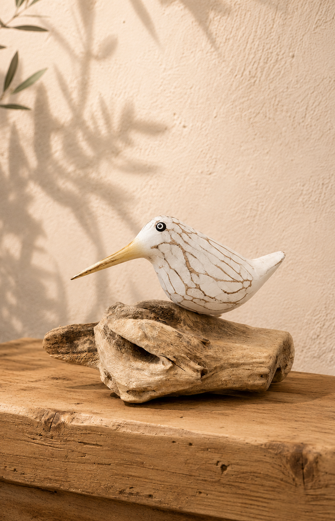 Oiseau blanc en bois sculpté avec bec jaune posé sur une branche de teck dans une ambiance bord de mer chic.