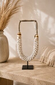 Collier décoratif en coquillages blancs sur pied métal noir dans une décoration bohème chic avec travertin et herbes séchées