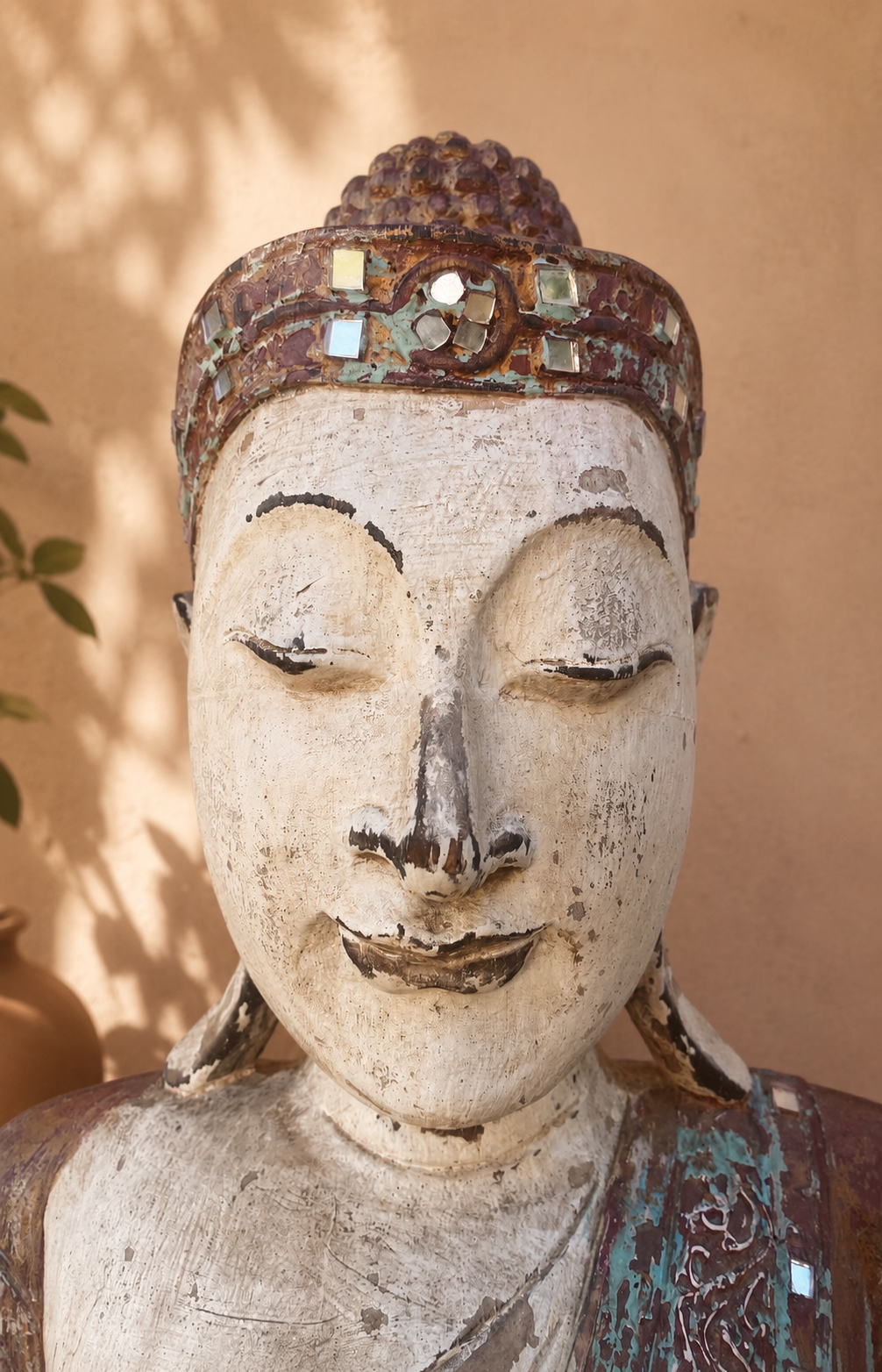 Détail du visage d’un Bouddha thaïlandais en bois patiné avec couronne ornée de petits miroirs