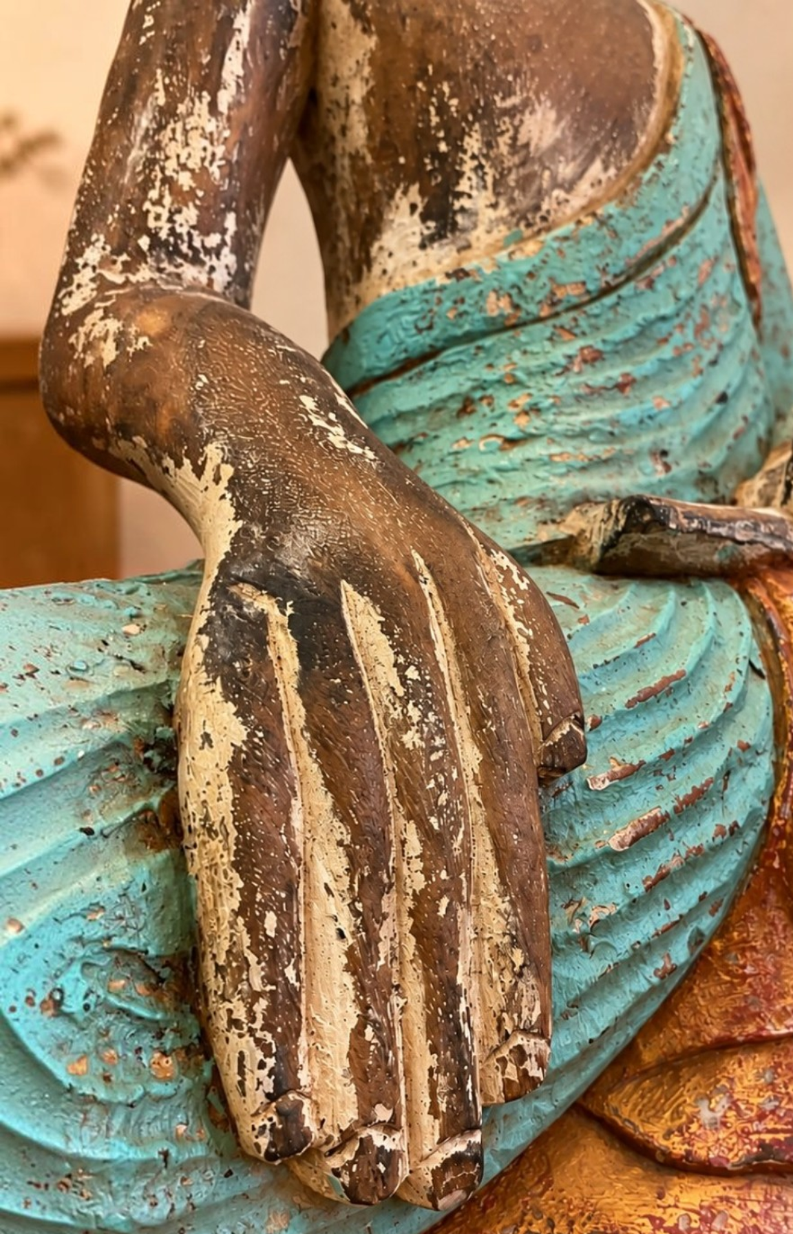 Gros plan sur les mains et la robe patinée d’un Bouddha en bois